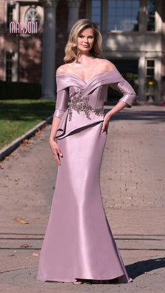 A woman stands outdoors on a paved pathway in front of a building, wearing the Marsoni MV1333 Long Formal Dress—a light purple off-the-shoulder evening gown with floral embellishments and a peplum bodice.