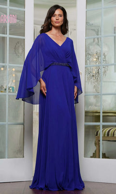 A woman stands indoors wearing the Long Formal Dress: Marsoni MV1350 in Electric Royal, featuring a floor-length chiffon design with sheer, flowing sleeves and an embellished waistbelt.