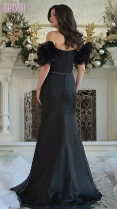 A woman in the Marsoni MV1353 long formal dress with off-shoulder ruffled sleeves stands elegantly before a decorated white fireplace.