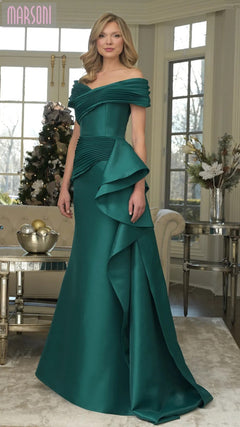 A woman stands indoors in the emerald Long Formal Dress: Marsoni MV1354, an off-shoulder mermaid gown with ruffled details, posed before a decorated Christmas tree and large windows.