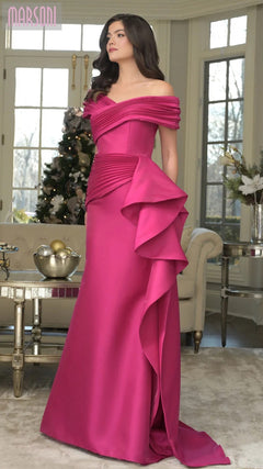 Indoors, a woman wears the Marsoni MV1354 long formal dress in fuchsia—an off-shoulder, floor-length mermaid gown featuring draped and pleated details.