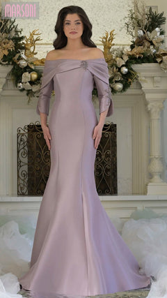 A woman stands indoors wearing the Marsoni MV1360 long formal dress in dusty rose, featuring a floor-length, off-the-shoulder design with a fitted bodice and brooch detail. Festive decorations are visible in the background.