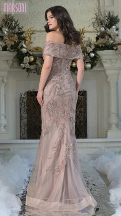 A woman wearing the Marsoni MV1372 long formal dress with a mermaid silhouette and delicate beaded embroidery stands before a decorated fireplace, elegantly glancing over her shoulder.