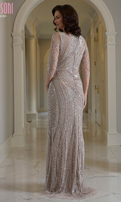 A woman wearing a Modest Long Formal Dress: Marsoni MV1380, featuring a long, beaded sequin evening gown with three-quarter sleeves, standing in a hallway.