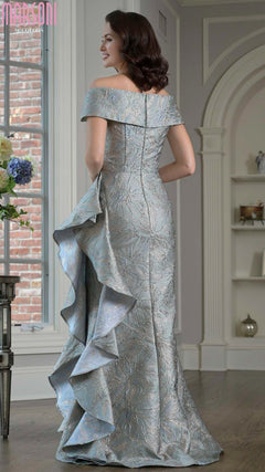 Indoors, a woman wears the Long Formal Dress: Marsoni MV1381, showcasing metallic brocade fabric, an off-the-shoulder neckline, and a cascading back ruffle detail.