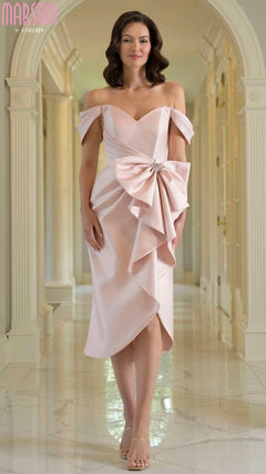 A woman stands in a hallway wearing the Marsoni MV1389 knee-length semi-formal dress in mauve with an off-the-shoulder design, oversized bow detail, and strappy heels.