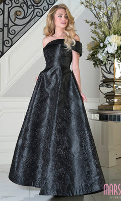 A woman wearing the Marsoni MV1395 black long formal dress stands indoors near a staircase and floral arrangement.