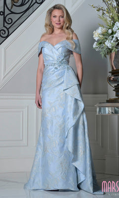 A woman in the Marsoni MV1401 long formal dress in powder blue, featuring off-the-shoulder style, floral patterns, and side draping, stands indoors near a white staircase and floral arrangement.