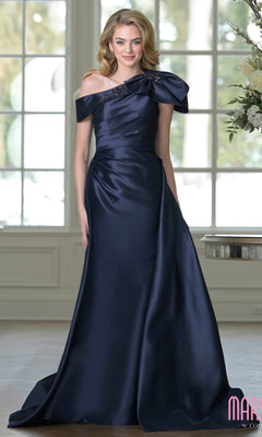 A woman stands indoors near a window and flowers, wearing the Marsoni MV1408 Long Formal Dress in Midnight, featuring a floor-length taffeta design with an asymmetrical off-the-shoulder neckline and ruched detailing.