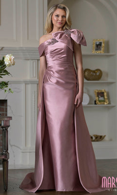 A woman stands in a room wearing the Marsoni MV1408 long formal dress in Rose Wood, featuring taffeta fabric, an asymmetrical neckline, a bold bow accent, and floral embellishment on one shoulder.