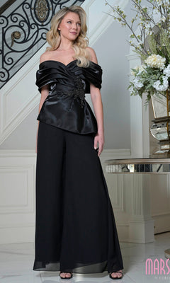 A woman stands indoors on a marble floor, wearing the Marsoni MV1410 long formal dress in black; floral arrangement and staircase in the background enhance her chic look.