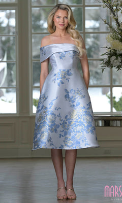 A woman wearing the Marsoni MV1415 knee-length semi-formal dress in Blue Multi stands indoors by large windows.