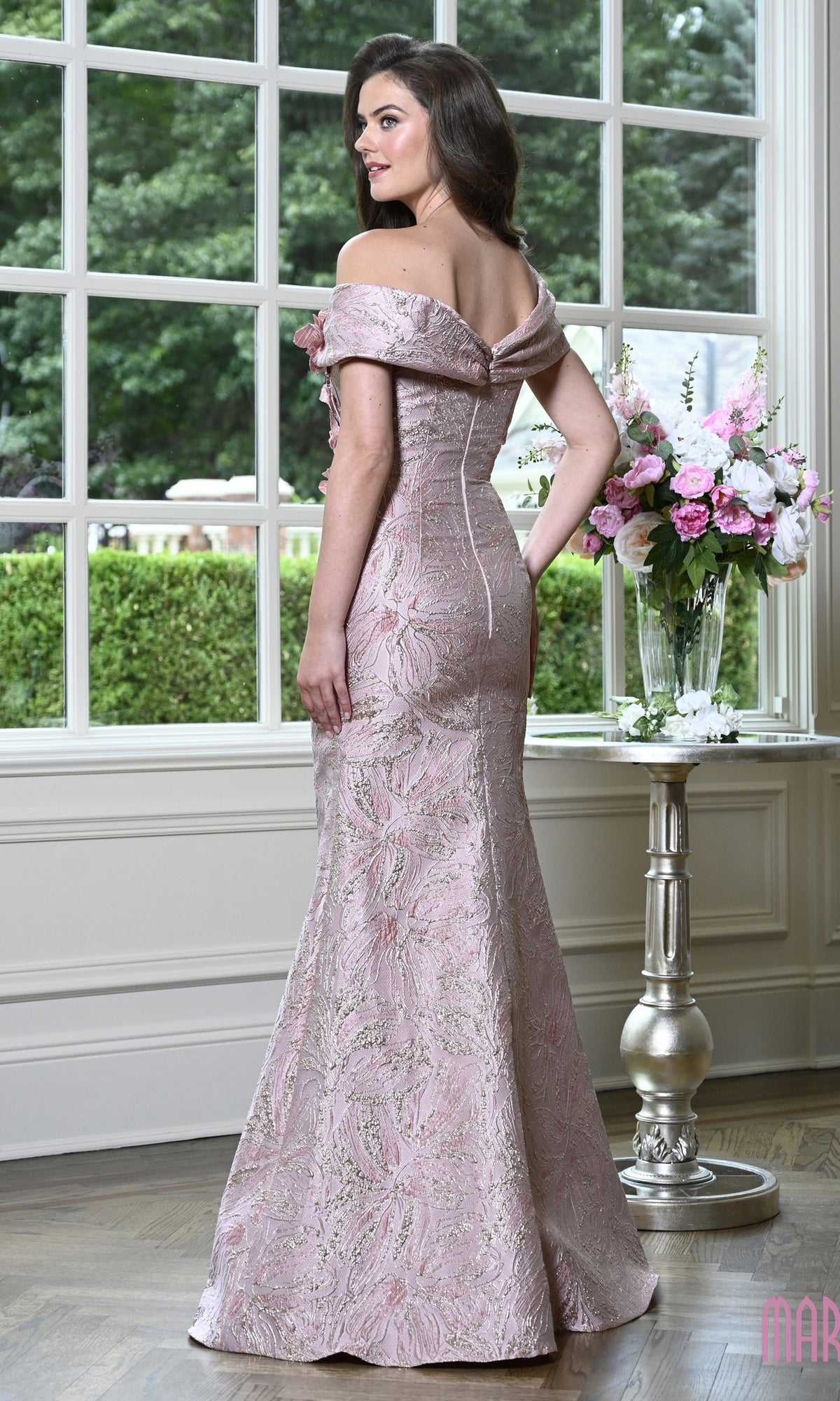 A woman wearing the Marsoni MV1422 long formal dress, a pale pink, off-the-shoulder, floor-length floral evening gown.