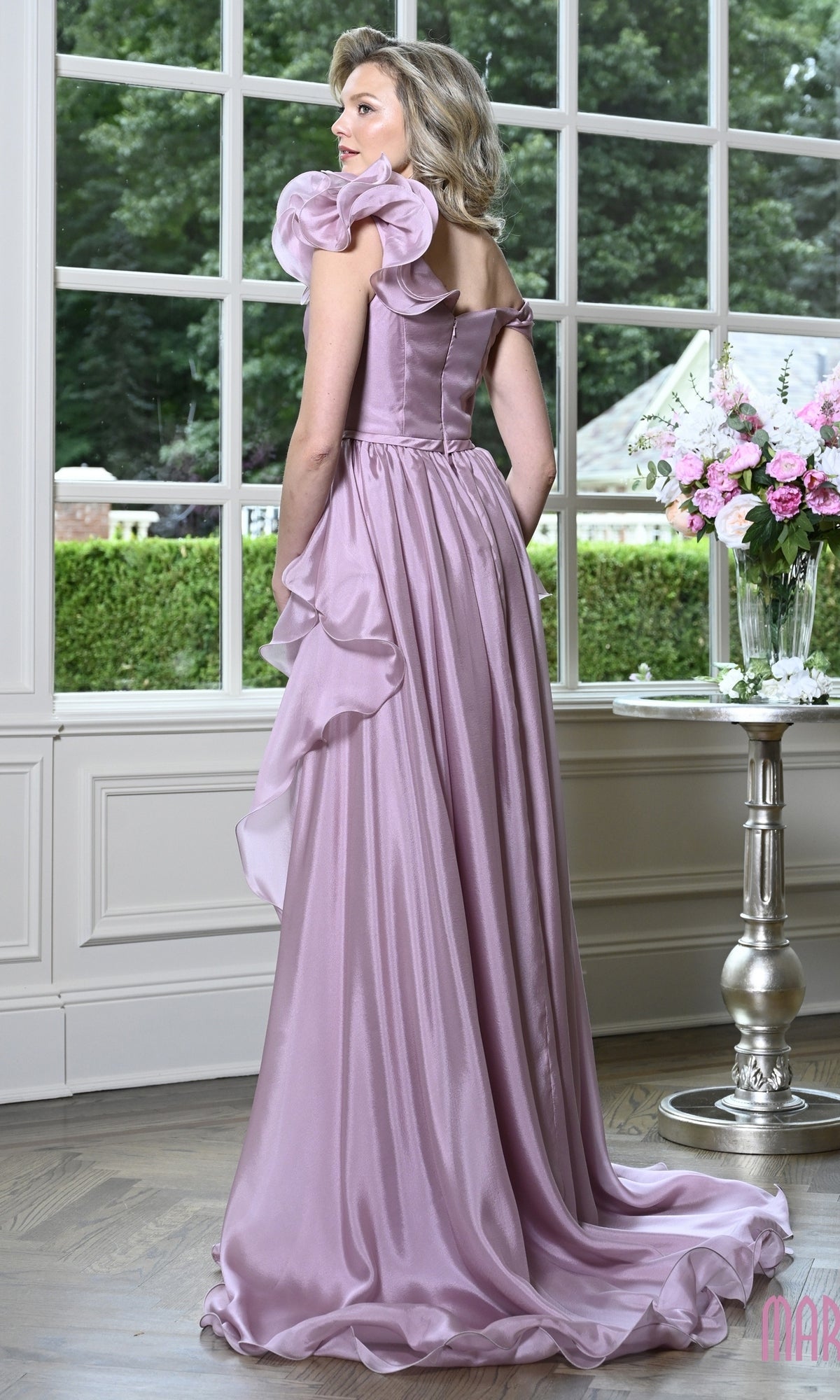 A woman standing in profile wearing a Long Formal Dress: Marsoni MV1425, a floor-length lavender ruffle evening gown with off-the-shoulder sleeves and a side-draped skirt.