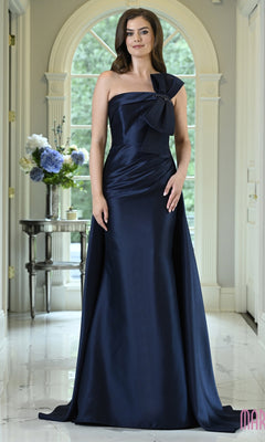 A woman wears a navy blue Long Formal Dress: Marsoni MV1431, a floor-length evening gown with a one-shoulder neckline and a decorative bow detail.