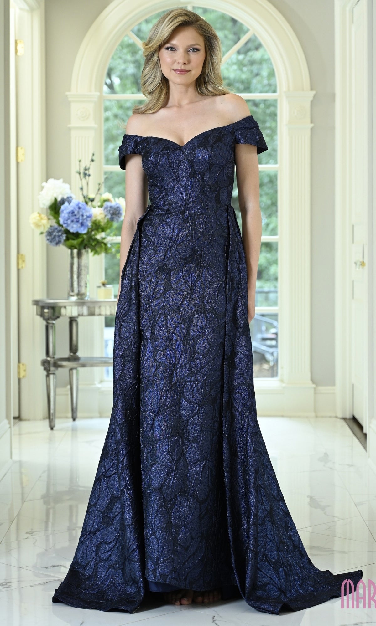 A woman wears a navy off-the-shoulder, floor-length floral jacquard Long Formal Dress: Marsoni MV1440 with a subtle brocade pattern.