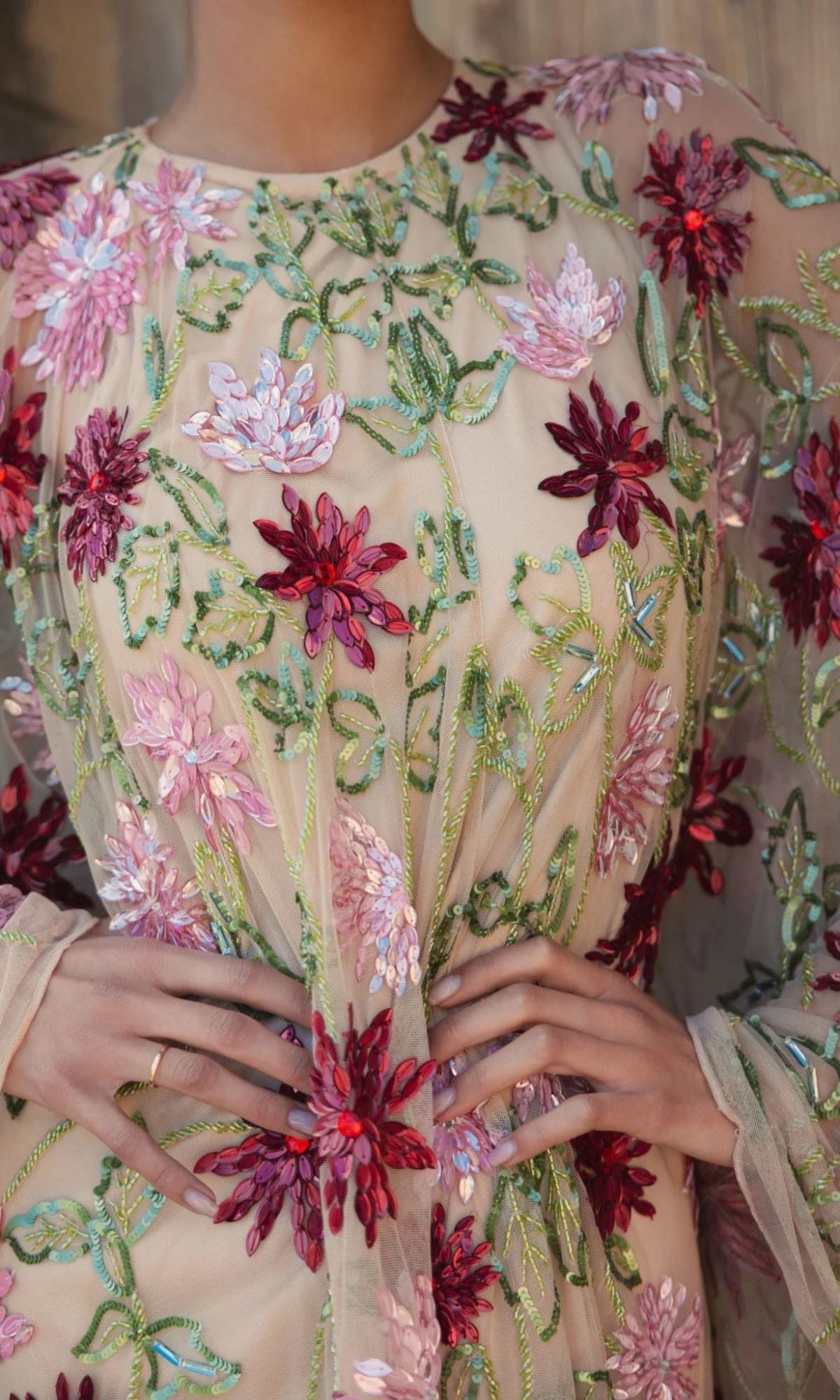 Close-up of a person wearing the Sequin Short Wedding Guest Dress: Mac Duggal 6123, featuring sheer fabric and intricate pink, red, and green floral embroidery, with their hands resting on their waist.