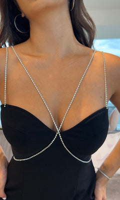 A woman wearing the Millionaire Black Mini Party Dress, featuring thin rhinestone straps and a sweetheart neckline, paired with hoop earrings.