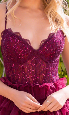 A woman wears the Velvi Lace-Corset Long Prom Ball Gown Morgan, a sleeveless, deep burgundy lace A-line dress with sequins and ruffle details, while standing outdoors.