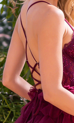 A person wearing the Velvi Lace-Corset Long Prom Ball Gown Morgan, a sleeveless, backless formal dress with thin crisscross straps and sequin details, standing outdoors.