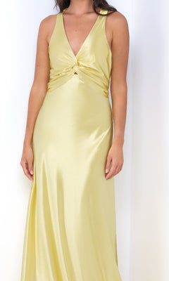 A woman wears the Odette by Velvi, a sleeveless satin long prom dress in light yellow with a floor-length silhouette, deep V-neckline, and elegant gathered detail at the empire waist.