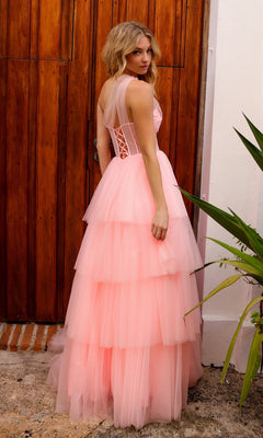 A woman in the Sheer-Bodice Long Layered Prom Ball Gown P1400 with a light pink tulle skirt stands outdoors by a wooden door, gazing over her shoulder.