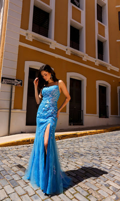 A woman wearing the Sequin-Floral Long Lace Prom Dress P1401 poses on a cobblestone street in front of a yellow building.
