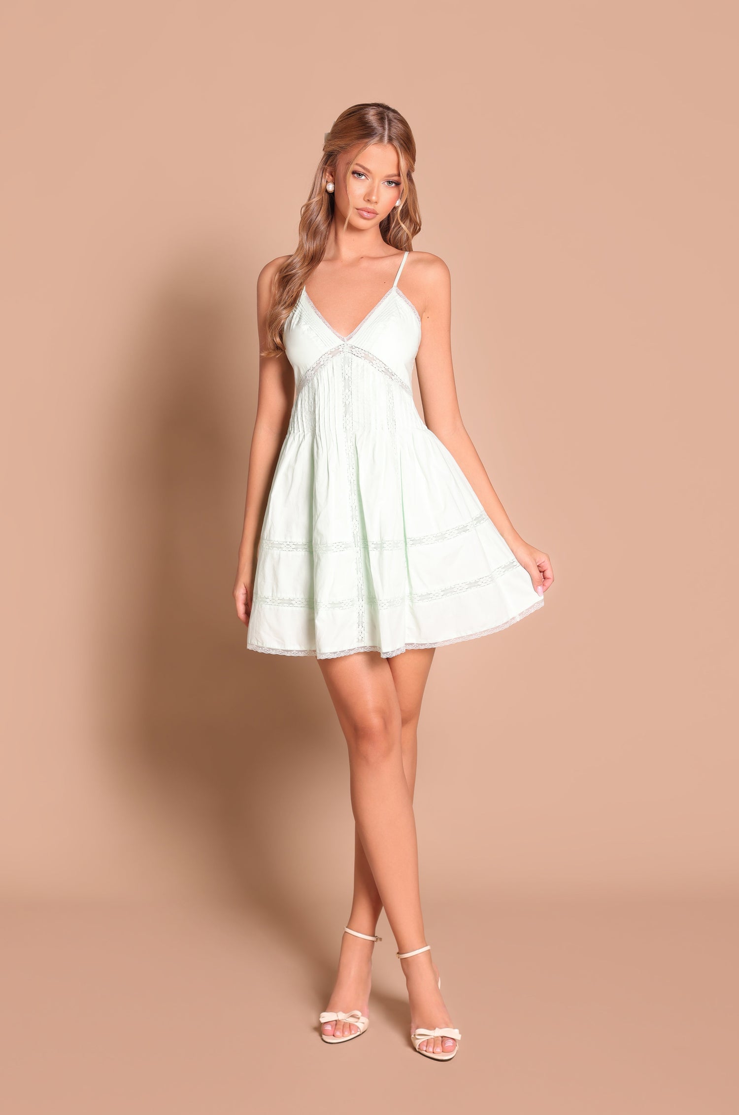 A woman wears the Valenia Mint Green V-Neck A-Line Mini Sundress with thin straps and white heels, standing against a plain beige background.