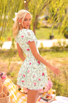 A woman with blonde hair in a ponytail wears the Analise Mint Green Short Casual Dress and stands outdoors near a picnic setup, looking over her shoulder.