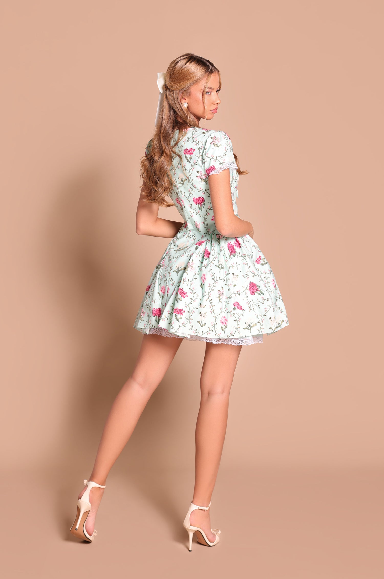 A woman poses with her back partially turned, wearing the Mint Green Short Casual Dress: Analise and high heels against a plain beige background.