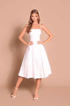 A woman wearing the Primrose Pink Simple Midi Casual Dress: Auberine and white heels stands against a beige background with her hands on her hips.