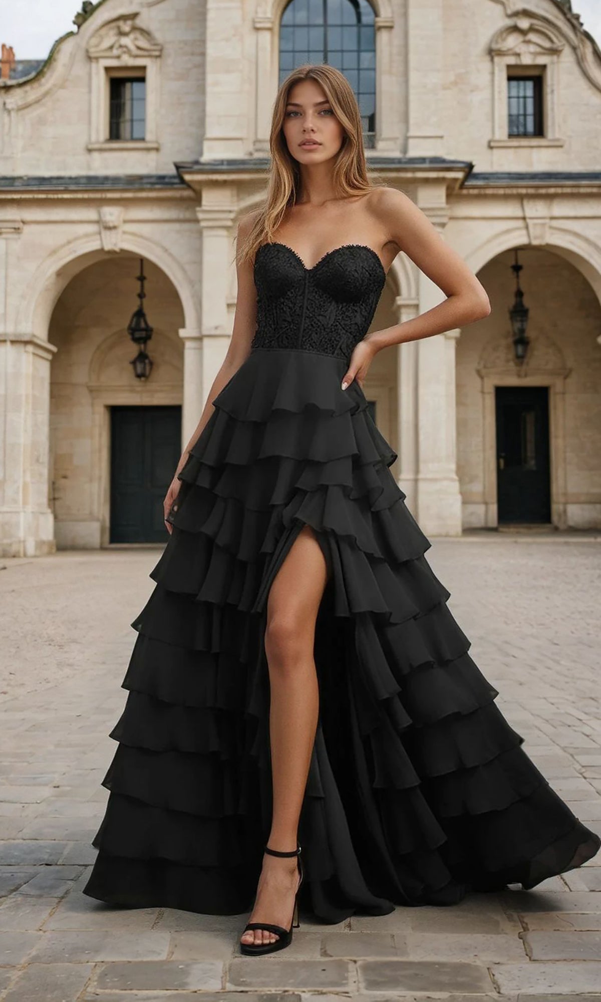 Woman wearing a black strapless gown with ruffled layers in front of an architectural building.
