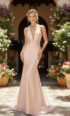 A woman stands outdoors among blooming flowers, wearing the PromGirl Exclusive Long Prom Dress with Embroidery in pale pink, featuring a halter neckline and mermaid silhouette.