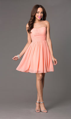 A woman stands against a gray background wearing the Sheer-Neck Short Wedding-Guest Party Dress 7006, paired with silver high-heeled sandals and a silver bracelet.