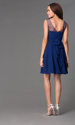 A woman stands facing away in the Sheer-Neck Short Wedding-Guest Party Dress 7006, a sleeveless, knee-length navy blue dress with a sheer back panel and large waist bow, paired with silver high heels.