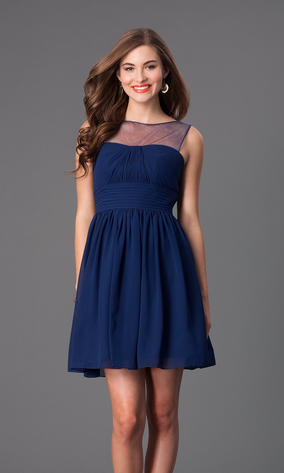 A woman smiles in the Sheer-Neck Short Wedding-Guest Party Dress 7006, a sleeveless navy blue cocktail dress with a sheer neckline, knee-length hem, and standing against a plain gray background.