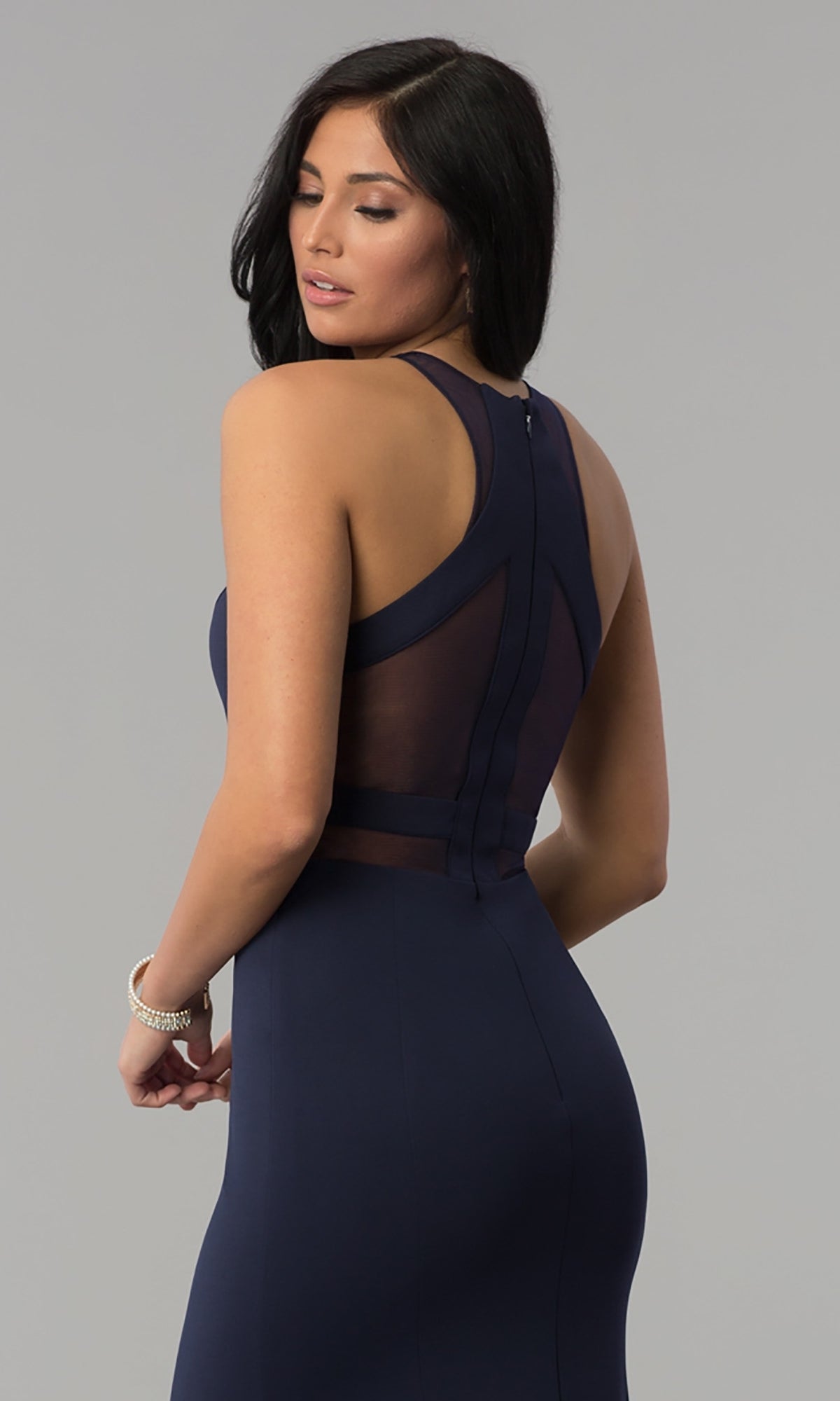 Woman models the Illusion-Cut-Out High-Neck Long Prom Dress 8054—sleeveless, navy blue, with sheer mesh back panels—standing and looking over her shoulder against a plain background.