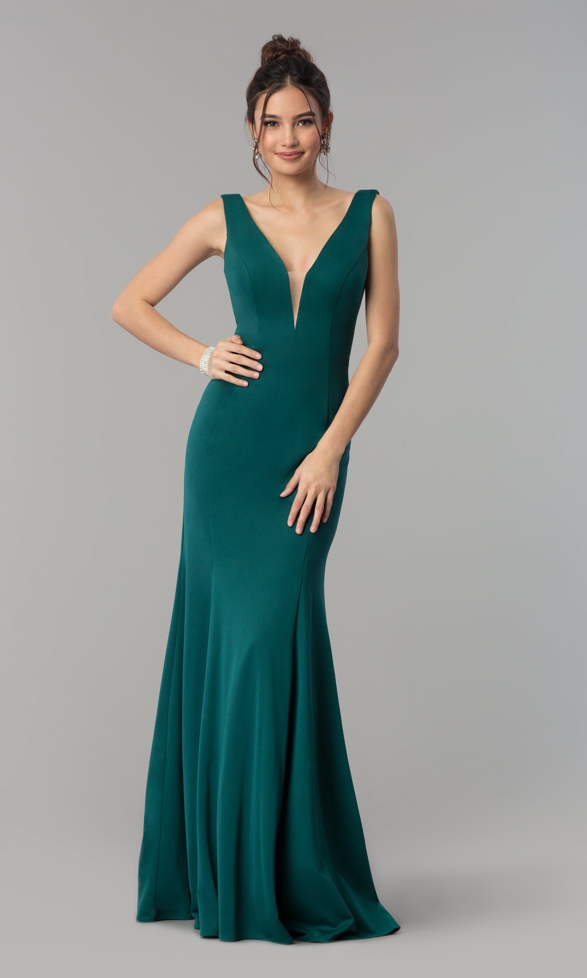 A woman models the Simple V-Neck Long Formal Jersey Prom Dress 8152 in green, featuring a sleeveless deep V-neck design, while standing against a plain gray background.