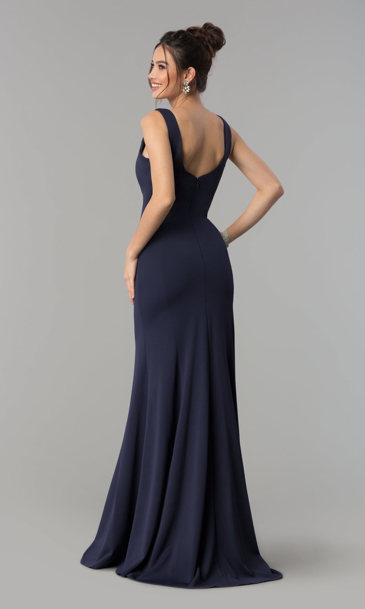 A woman poses in the Simple V-Neck Long Formal Jersey Prom Dress 8152, a sleeveless, floor-length navy gown with a deep V-back, against a plain light gray background.