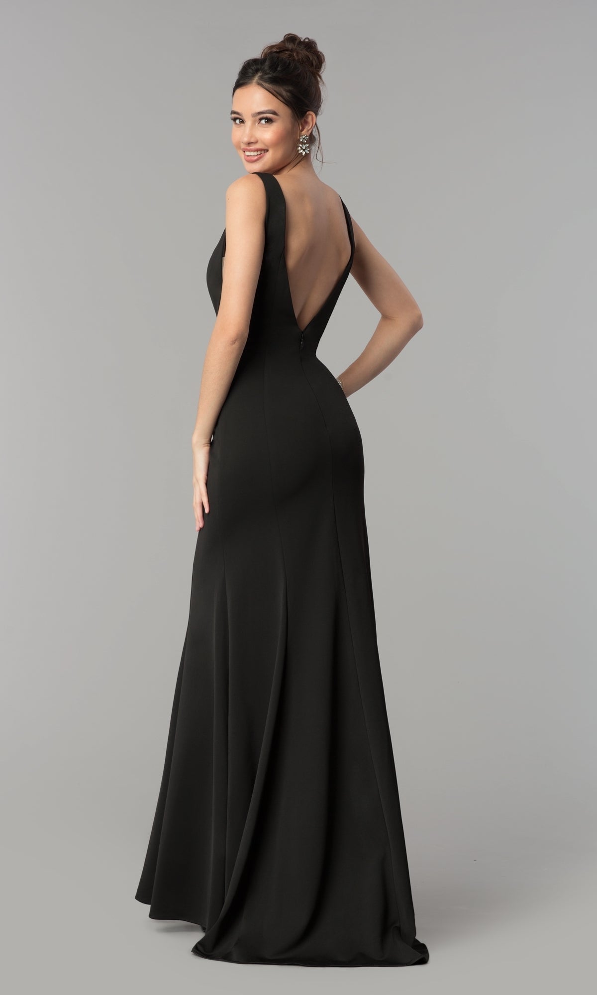 A woman smiles over her shoulder in the Sleeveless V-Neck Long Formal Prom Dress 8158, a floor-length gown with a deep V-back, set against a plain gray background.