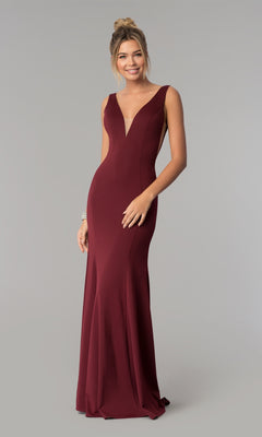 A woman stands against a plain gray background wearing the Sleeveless V-Neck Long Formal Prom Dress 8158 in burgundy, featuring a floor-length silhouette and plunging neckline.