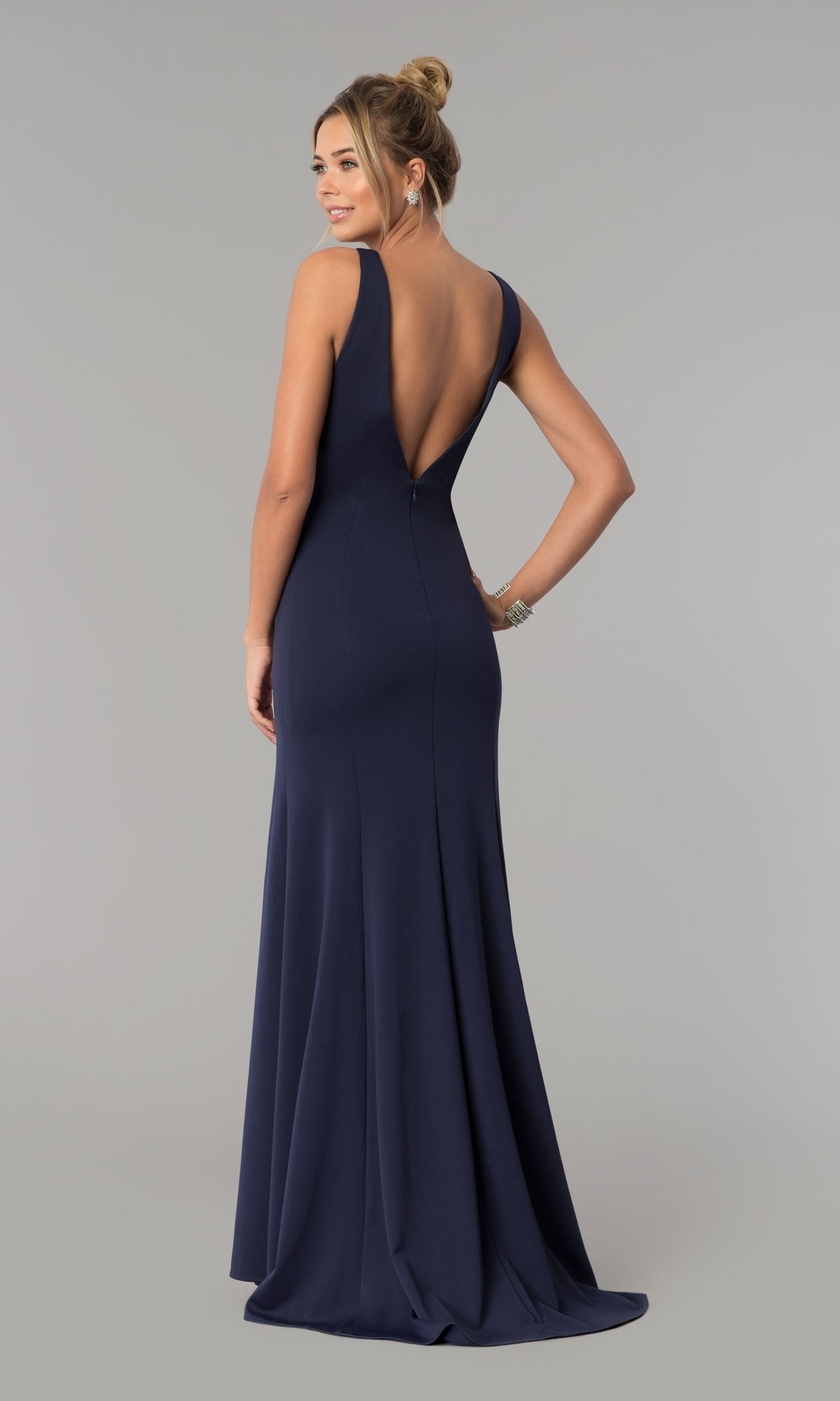 A woman models the Sleeveless V-Neck Long Formal Prom Dress 8158 in navy blue, featuring a deep V-back, as she stands facing away against a plain gray background.
