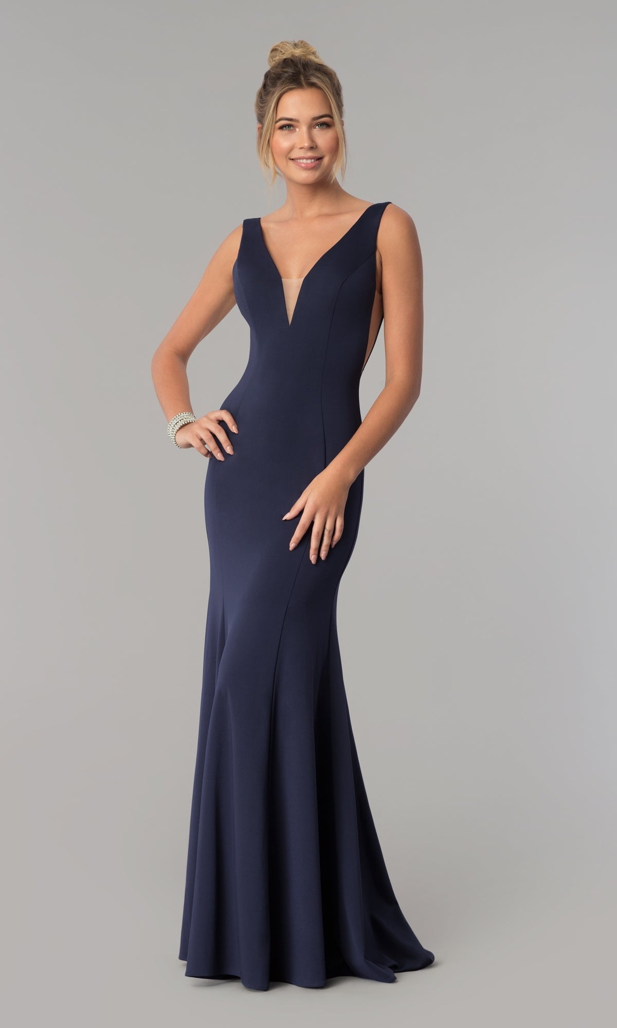A woman stands smiling against a plain background, wearing the Sleeveless V-Neck Long Formal Prom Dress 8158 in navy blue, featuring a deep neckline and floor-length design.