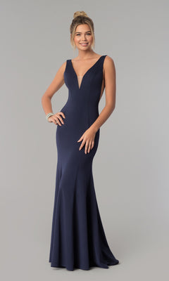 A woman stands smiling against a plain background, wearing the Sleeveless V-Neck Long Formal Prom Dress 8158 in navy blue, featuring a deep neckline and floor-length design.