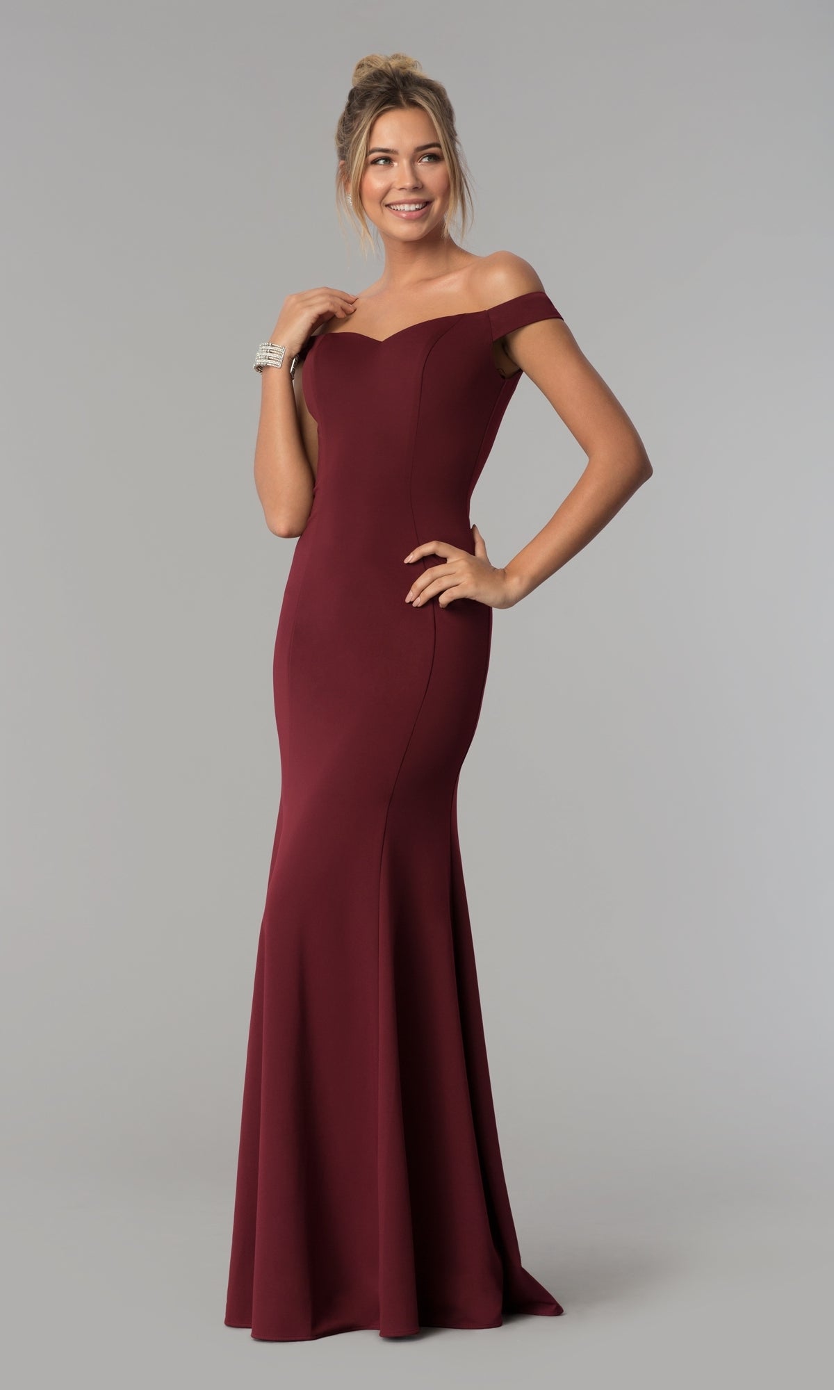 A woman in the Simple Off-the-Shoulder Long Formal Prom Dress 8160, burgundy, stands against a plain light gray background, smiling with one hand on her hip.
