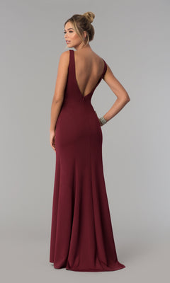 A woman stands facing away against a plain gray background, wearing the Sheer-Sided Backless Long Formal Prom Dress 8168—a sleeveless, floor-length burgundy jersey dress with a deep V-back.