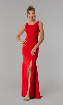 A woman stands and smiles against a plain gray background, wearing the Sheer-Sided Backless Long Formal Prom Dress 8168—a sleeveless, floor-length red gown with a thigh-high slit.