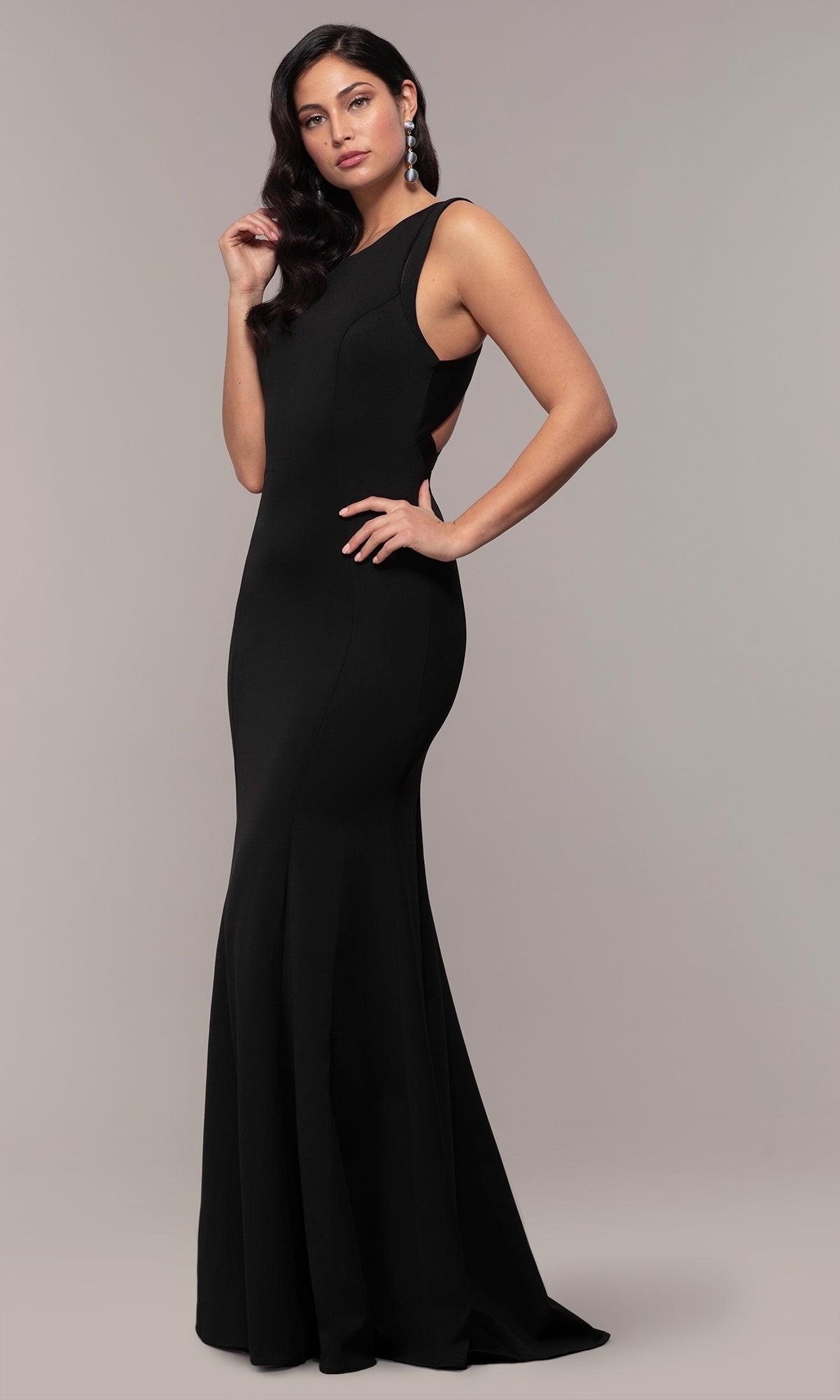 A woman poses against a plain background in the Strappy-Open-Back Long Formal Prom Dress 8232—a sleeveless, floor-length black gown with a fitted bodice, slight mermaid silhouette, and strappy open back.