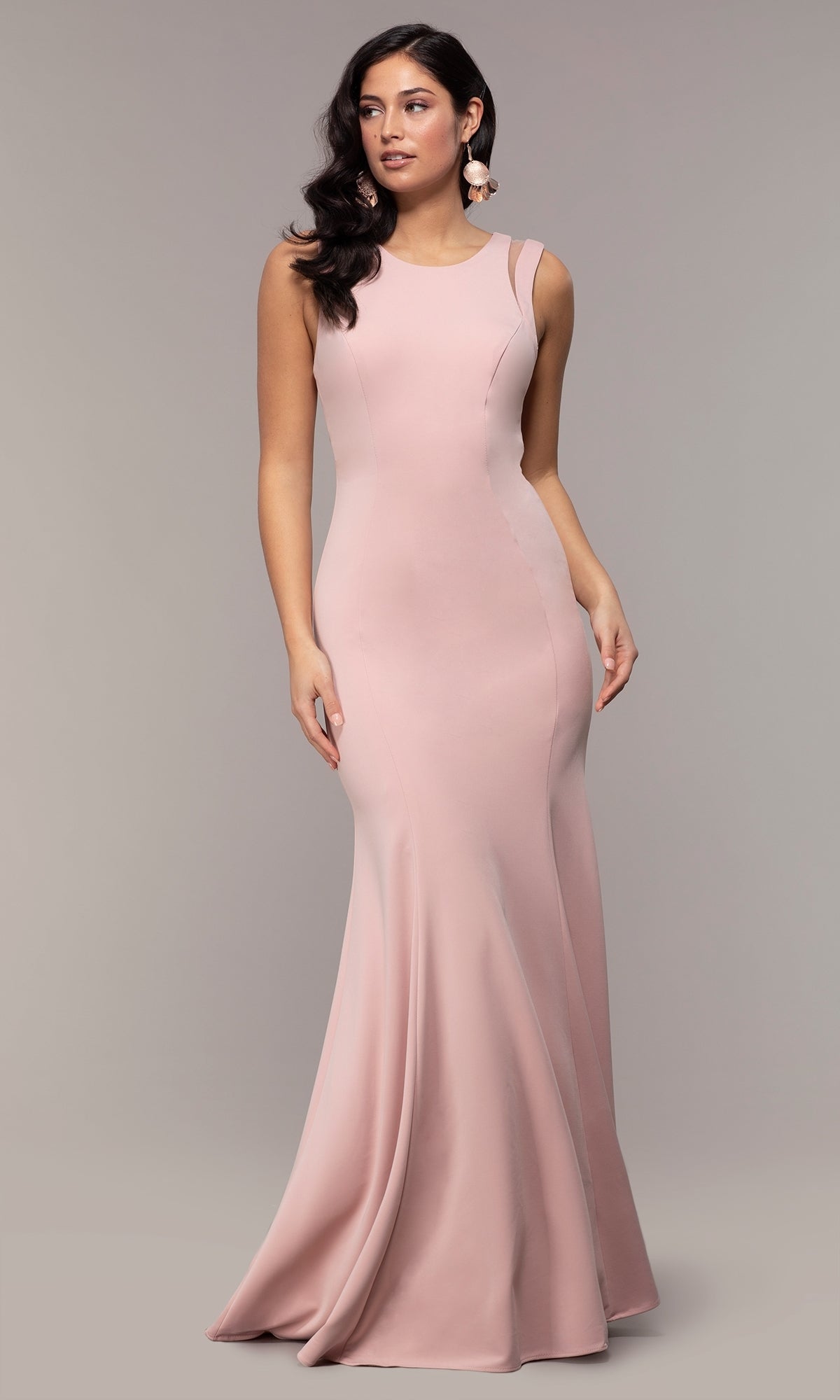 A woman in the Strappy-Open-Back Long Formal Prom Dress 8232—sleeveless, blush pink, floor-length with a fitted bodice and flared skirt—stands against a plain grey background.