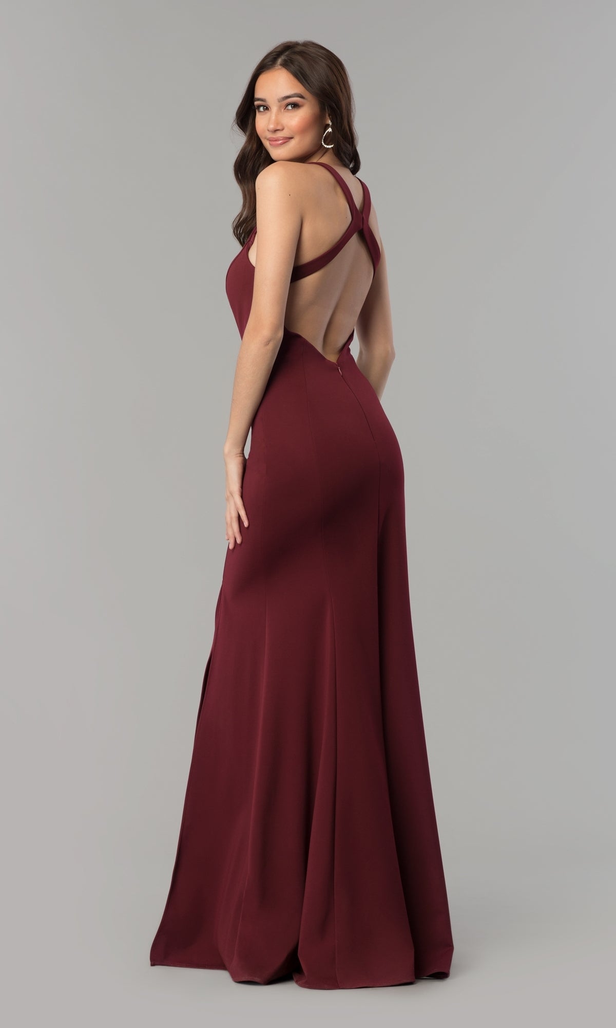 A woman models the Simple Sleeveless Long Jersey Prom Dress 8298—maroon, open-back, with a crisscross design—standing and glancing over her shoulder against a plain background.